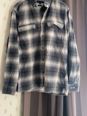 Rutig skjorta från Tommy Hilfiger - Snygg långärmad skjorta från Tommy Hilfiger i svart och vitt rutigt mönster. Skjortan har två bröstfickor med lock och knäppning framtill. Perfekt för en avslappnad och trendig stil.