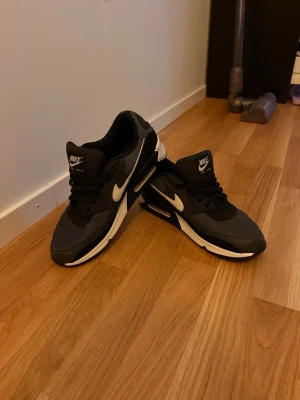 Nike Air Max 90 svart/vit sneaker - Snygga Nike Air Max 90 sneakers i svart med vita detaljer och sula. Klassisk låg modell med mesh och syntetmaterial för bra komfort och stil. Perfekta för dig som gillar streetwear och sportig look. Ikonisk Nike-logga på sidan och tungan.