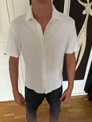 Vit kortärmad skjorta med knappar - Snygg vit skjorta med korta ärmar och klassisk krage. Skjortan har knäppning framtill och en clean, stilren look som passar till jeans eller chinos. Perfekt för dig som gillar enkel och fräsch stil.