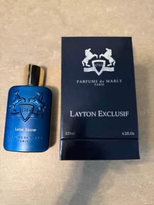 Layton Exclusif parfym 125ml - Lyxig parfym från Parfums de Marly, Layton Exclusif, i en snygg mörkblå flaska med guldfärgat lock och detaljer. Flaskan rymmer 125 ml och har en elegant design med reliefmönster. Har endas använt 5 ml