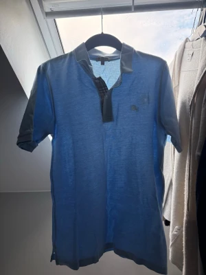 Blå kortärmad skjorta från Burberry - Säljer farsans gamla Burberry tröja som ja fick häromdagen, med klassiskt rutigt tyg på insidan av knappslån. Skjortan har en liten broderad logga på bröstet och kontrastfärgade detaljer vid krage och ärmslut. Perfekt för en stilren och avslappnad look. Det står S men men är för lång på en 180 grabb, skriv om ni har frågor👊🔥