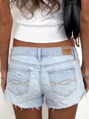 Ljusblå jeansshorts Abercrombie & Fitch - Säljer ett par ljusblå jeansshorts från Abercrombie & Fitch med råa kanter och slitna detaljer. W26