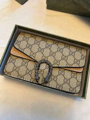 Gucci beige kuvertväska med GG-mönster - Säljer en beige kuvertväska  Gucci med klassiskt GG-mönster och snyggt silverfärgat spänne framtill. Är du intresserad skriv för mer info 