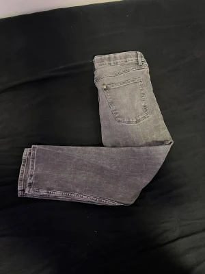 Grå tvättade raka jeans - Säljer ett par grå jeans med tvättad look och raka ben. Jeansen har klassisk femficksdesign och normal midja. Materialet är denim i bomull och de har en avslappnad passform som passar till många olika stilar.