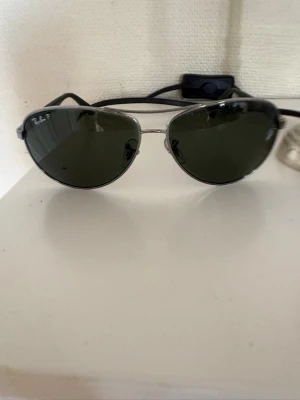 Ray-Ban polarized solglasögon  - Klassiska Ray-Ban solglasögon med silvrig metallbåge och mörkgröna linser. Tidlös design med tunna skalmar och Ray-Ban-logga på sidan. Perfekta för dig som vill ha en ikonisk och stilren look.