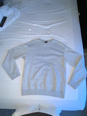 Ljusgrå basic sweatshirt - En stilren ljusgrå sweatshirt med rund halsringning och ribbade muddar vid ärmslut och nederkant. Perfekt för en avslappnad look och enkel att matcha med andra plagg. Tillverkad i mjukt material för extra komfort.