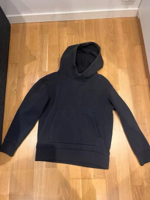 Svart hoodie från sail racing - En stilren svart hoodie från sail racing med stor huva och rymlig magficka. Hoodien har en klassisk passform med ribbade muddar vid ärmslut och nederkant. Perfekt för en avslappnad look och enkel att matcha med andra plagg.