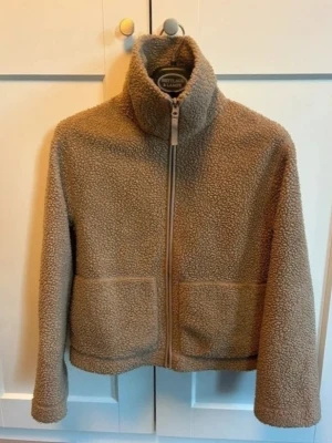 Snygg teddyjacka från H&M Stl S - Priset är inte förhandlingsbart. En jättefin och mysig teddyjacka från H&M i storlek S, med dragkedja framtill och två fickor. Jackan har en hög krage, i mycket bra skick då den endast är sparsamt använd. Perfekt till hösten eller som ett mysigt lager på lagret-plagg!  Mått: axel till axel 48cm amhålla till amhålla 46cm längd 59cm.