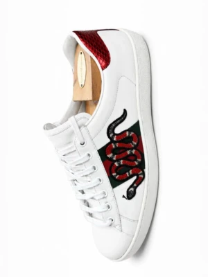 Gucci Ace sneakers med orm - Gucci Ace sneakers i vitt läder med ikonisk broderad orm på sidan och gröna/röda detaljer. Baksidan har metallicrött och metallicgrönt ormskinnsmönster. Klassisk låg modell med vita snören och gummisula. Perfekta för dig som vill sticka ut.