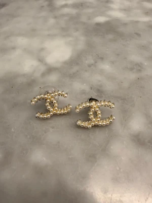 Pärlörhängen i CC-form - Säljer ett par örhängen formade som två sammankopplade CC, täckta med små vita pärlor.