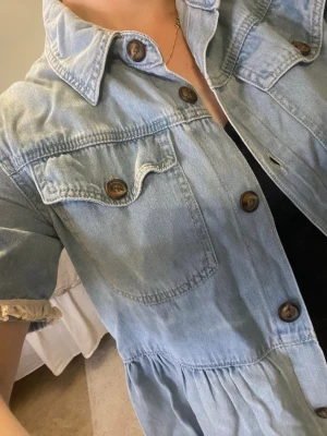  jeansjacka med kort ärm - Trendig ljusblå jeansjacka med korta ärmar och snygga bruna knappar. Jackan har klassisk krage, bröstficka med lock och avslappnad passform. Perfekt att slänga över en t-shirt för en cool look. Man kan använda den som jacka eller som tröja. 