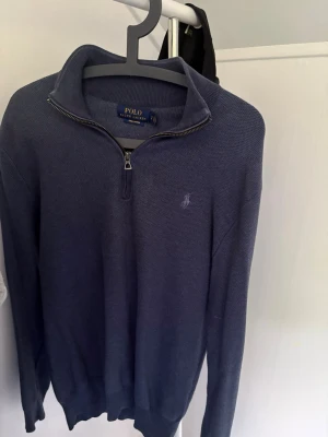 Blå halvzip tröja från Polo Ralph Lauren - Mörkblå stickad tröja från Polo Ralph Lauren i mjuk pima cotton. Tröjan har halv dragkedja, hög krage och diskret broderad logga på bröstet. Perfekt för en stilren och avslappnad look. I mycket bra skick, säljes för 350 kr 
