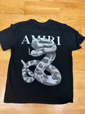 Svart amiri t shirt - Svart t-shirt från Amiri med stort vitt ormtryck och logga på ryggen. Klassisk rund hals och korta ärmar. T-shirten har en loose passform och är tillverkad i mjuk bomull, perfekt för en avslappnad och cool stil.