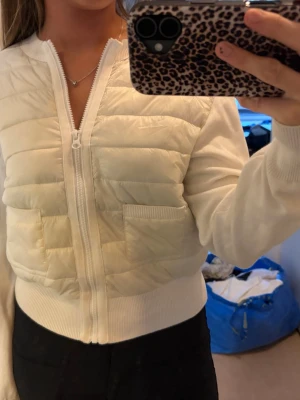 Vit quiltad cardigan med dragkedja - Säljer en vit cardiganjacka med quiltade partier framtill och två fickor. Jackan har dragkedja hela vägen, ribbade muddar och är tillverkad i en mix av vadderat och stickat material. Perfekt för en chill och stilren look.