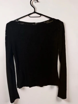Svart spets  långärmad topp - Snygg svart långärmad topp i mesh med diskret mönster. Toppen har en tight passform och är perfekt att styla lager på lager. Tunt och stretchigt material som ger en cool look. (PRIS LAPP KVAR)