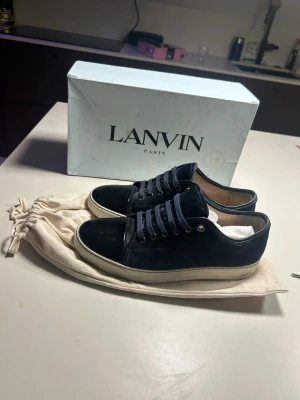 Svarta sneakers från Lanvin - Snygga svarta sneakers från Lanvin med ovandel i mocka och tåparti i blankt läder. Skorna har vita sulor och matchande svarta skosnören. Klassisk låg modell som passar till många olika stilar. Priset kan diskuteras vid en snabb affär!!! Uk size 8 funkar även i 9