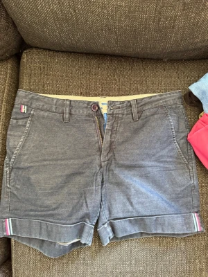 Gråa shorts med uppvikta ben - Snygga grå shorts med uppvikta ben och bälteshällor. Shortsen har två sidofickor fram och två bakfickor. Detaljer med små färgade band vid bensluten och knappstängning framtill. Perfekta för varma dagar.  Skriv privat för fler bilder eller om du har några frågor💗