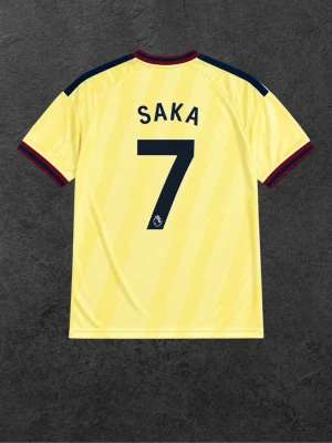 Arsenal Saka 7 gul matchtröja 26/27 tredje - Gul Arsenal matchtröja med SAKA och nummer 7 på ryggen. Tröjan har mörkblå detaljer på axlar och ärmslut, samt röda inslag vid krage och ärmar. Adidas-logga och Arsenal-emblem på bröstet, samt Emirates Fly Better-tryck framtill.