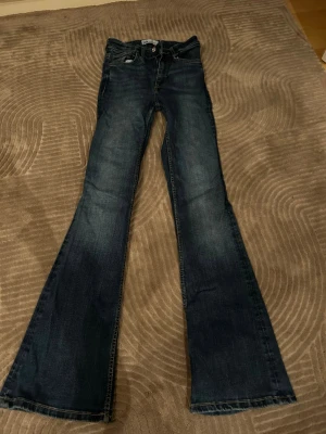 Mörkblå bootcut jeans - Säljer ett par mörkblå bootcut jeans med klassisk femficksmodell och lätt slitna detaljer. Jeansen har utsvängda ben och är tillverkade i denim med snygg tvätt. Perfekta för dig som gillar retrostil och vill ha ett par jeans som sticker ut.