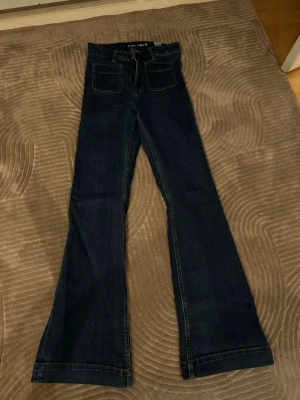 Mörkblå bootcut jeans - Säljer ett par mörkblå bootcut jeans med hög midja och klassiska fickor både fram och bak. Köpte från BiKBoK, storleken är CAMILLE W26 L32