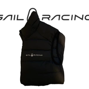 Svart dunväst från Sail Racing - Snygg svart dunväst från Sail Racing med diskret logga på bröstet. Västen har en quiltad design, dragkedja framtill och hög krage. Perfekt för lager-på-lager och håller dig varm under de kyliga dagar som snart kommer. Materialet är dunfyllning för extra värme.