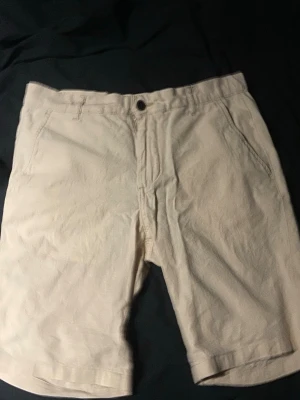 Jack and Jones shorts - Snygga beige shorts med klassisk passform och bälteshällor. De har två sidofickor fram och två bakfickor med minimalistisk design. Perfekta för varma dagar och enkla att matcha med olika stilar.