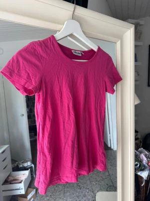 Rosa t-shirt från Tribute - En enkel och snygg rosa t-shirt från Tribute i mjuk bomull. Klassisk rund halsringning och korta ärmar. Perfekt basplagg att matcha med jeans eller kjol för en avslappnad look.