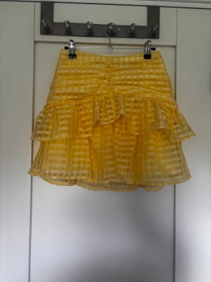 Gul rutig volangkjol - Söt gul kortkjol med rutigt mönster och dubbla volanger. Kjolen har en lätt transparent look och är perfekt för sommarens alla tillfällen. Materialet känns luftigt och bekvämt, och volangerna ger en extra touch av stil. Helt ny