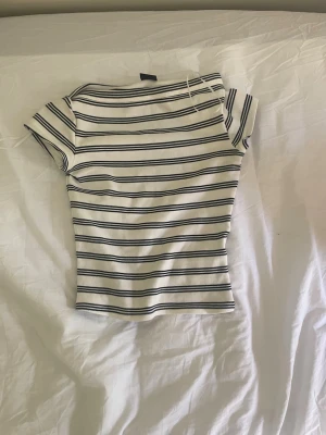 Randig vit och blå ribbad topp - Säljer en kortärmad topp med smal passform i vitt med marinblå horisontella ränder. Toppen har rund halsringning och är ribbad i materialet vilket ger en snygg och bekväm look. I storlek xs.apris kan diskuteras😁