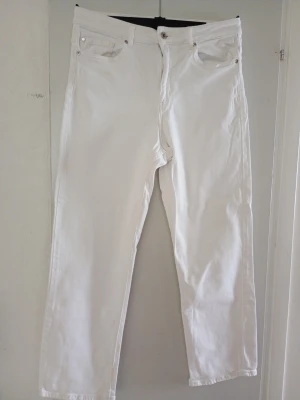 Vita raka jeans med fem fickor - Säljer ett par vita jeans med rak passform och klassisk femficksdesign. Jeansen har normal midja, bälteshällor och stängs med knapp och dragkedja. Materialet är kraftigt och känns som bomullsdenim. Perfekta för en clean och fräsch look.