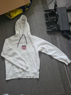 Vit GANT Hoodie - Helt vanlig vit hoodie från GANT med en stor logga över bröstet. Magficka finns. Storlek L. Mycket bra skick. 
