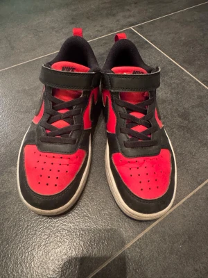Nike sneakers röd och svart, barn - Snygga sneakers från Nike i rött och svart med klassisk swoosh på sidan. Skorna har kardborreband, svarta skosnören och vit sula. 