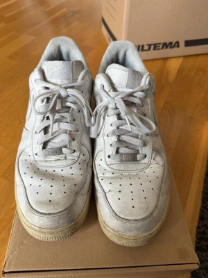 Vita Nike Air Force 1 sneakers - Klassiska vita Nike Air Force 1. Skorna har perforerad tå, vit ovandel i läder och den ikoniska swoosh-loggan på sidan. 