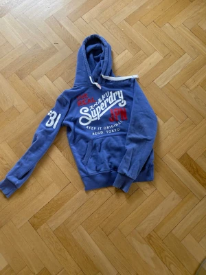 Blå Superdry Hoodie - En blå superdry hoodie i perfekt skick. Inga defekter överhuvudtaget.     Tveka inte på att höra av dig om du har några frågor.