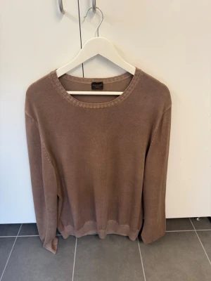 Beige stickad tröja Rose & Born, stl XL - Snygg beige stickad tröja från Rose & Born. Tröjan har rund halsringning, långa ärmar och ribbade muddar vid hals, ärmslut och nederkant. Perfekt basplagg i garderoben och enkel att matcha till olika outfits.