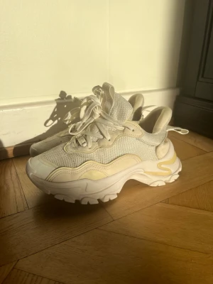 Sneakers - Säljer ett par chunky vita sneakers med tjock sula och meshdetaljer. Skorna har inslag av beige och krämfärgade partier samt en markerad sula för extra attityd. Skorna är i använt skick men har mer att ge.