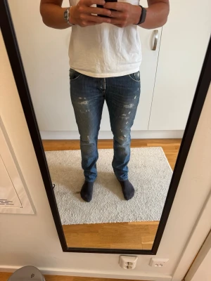 Dondup jeans ”Sam” - Säljer ett par blå Domdup jeans med slitningar och raka ben. Jeansen har klassisk femficksmodell och snygga detaljer med slitna partier framtill och baktill. Säljer då mina ben blivit för stora. Storlek 34 men passar även folk med 32&33. Modellen heter ”Sam”