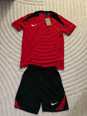 Nike röd och svart träningsset - Röd och svart träningsset från Nike. Storlek M, helt ny och oanvänd. Perfekt nu under sommarn och för träning. Fraktas inom 24 timmar📦🚛