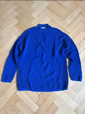 Blå ribbad tröja från Weekday - Säljer en blå långärmad tröja från Weekday i ribbat material. Tröjan har en avslappnad passform, liten ståkrage och diskreta sömmar längs sidorna. Perfekt för dig som gillar minimalistisk och modern stil. Modellen är oversize. 