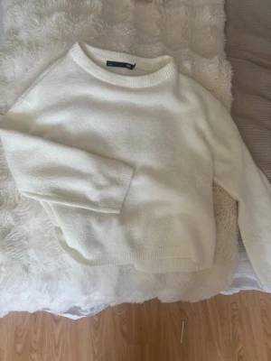 Vit stickad tröja med rund hals - Klassisk vit stickad tröja med rund halsringning och långa ärmar. Tröjan har en avslappnad passform och ribbade muddar vid ärmslut och nederkant. Perfekt att matcha med jeans eller kjol för en enkel och stilren look.