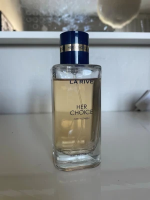 La Rive Her Choice Eau de Parfum - La Rive Her Choice Eau de Parfum för kvinnor i en stilren, rektangulär glasflaska med blått och guldigt lock. Perfekt för dig som gillar eleganta och feminina parfymer.