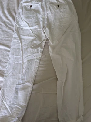 Vita linnebyxor med raka ben - Säljer ett par vita linnebyxor från H&M i storlek S. Byxorna har raka ben, resår i midjan och två bakfickor med knapp. Perfekta för en avslappnad och stilren look under varma dagar.