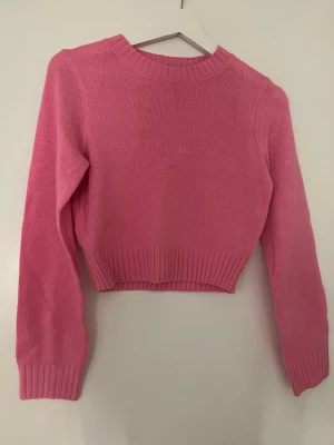 Rosa cropped stickad tröja Divided - Snygg rosa stickad tröja från Divided med croppad passform och ribbade muddar vid ärmslut, nederkant och halsringning. 