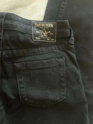Svarta jeans från True Religion - Snygga svarta jeans från True Religion med klassisk logga på bakfickan och raka ben. Jeansen har fem fickor och tydliga sömmar, tillverkade i ett mjukt och slitstarkt material. Perfekta för dig som vill ha en stilren och trendig look. Modellen heter BOBBI baggy 🔥 storleken är W24, innerbenslängden är 82cm 💫🌟