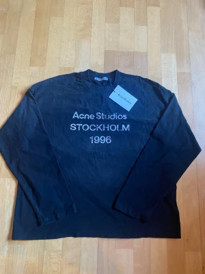Svart långärmad topp Acne Studios - Svart långärmad topp från Acne Studios med tryck 'Acne Studios STOCKHOLM 1996' framtill. Klassisk rund halsringning och relaxed fit. Perfekt för dig som gillar stilrena och trendiga plagg med en urban touch.