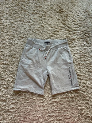 Grå shorts med snörning Tommy Hilfiger - Snygga grå shorts från Tommy Hilfiger med snörning i midjan och två sidofickor. Mjuk resår i midjan och diskret logga tryckt på ena benet. Baksidan har en ficka med dragkedja. Perfekta för chill dagar eller träning.