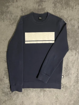 BOSS Hugo Boss – Navy Sweatshirt (S) - Premium Hugo Boss sweatshirt in deep navy blue, featuring a stylish white embossed logo panel across the chest. Size S, fits well also for M. Length 67 cm, pit-to-pit 50 cm – modern and comfortable fit.  ✅ Condition: Excellent – no visible wear or stains 💯 Authenticity: 100% genuine Hugo Boss garment 📦 Shipping: Fast dispatch after purchase  This sweatshirt combines minimalist elegance and high-end craftsmanship, making it a perfect choice for those who appreciate refined, timeless style 💙