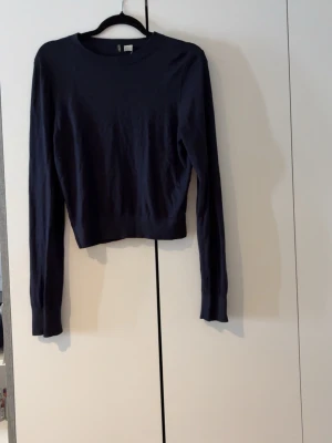 Mörkblå tröja från H&M - En enkel och stilren mörkblå tröja från H&M med rund halsringning och långa ärmar. Tröjan har ribbade muddar vid hals, ärmslut och nederkant. Perfekt att matcha med jeans eller kjol för en clean look.