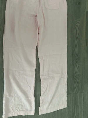 Ljusrosa linnebyxor med raka ben - Säljer ett par ljusrosa linnebyxor med raka ben och resår i midjan. Byxorna har sidfickor fram och en bakficka. Perfekta för en avslappnad och trendig look. Materialet är svalt och luftigt linne. Har ej använts. 
