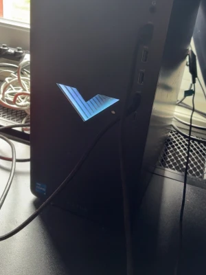 HP Victus stationär gamingdator - Säljer en svart HP Victus stationär dator med stilren design och blått lysande V-logga på framsidan. Chassit är i metall och har flera USB-portar på sidan. Perfekt för gaming och kreativa projekt.